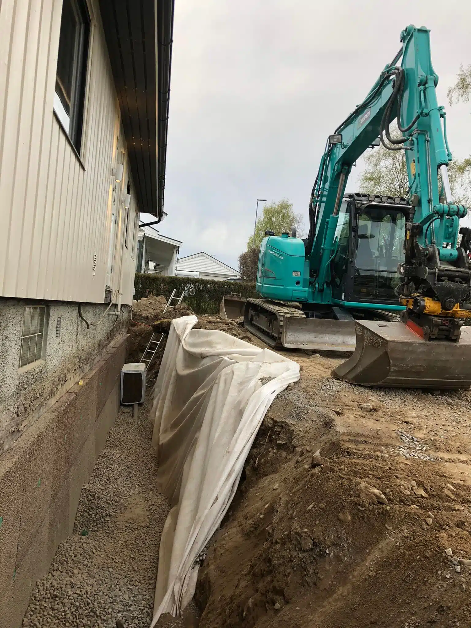 Gravemaskin graver drenering rundt hus